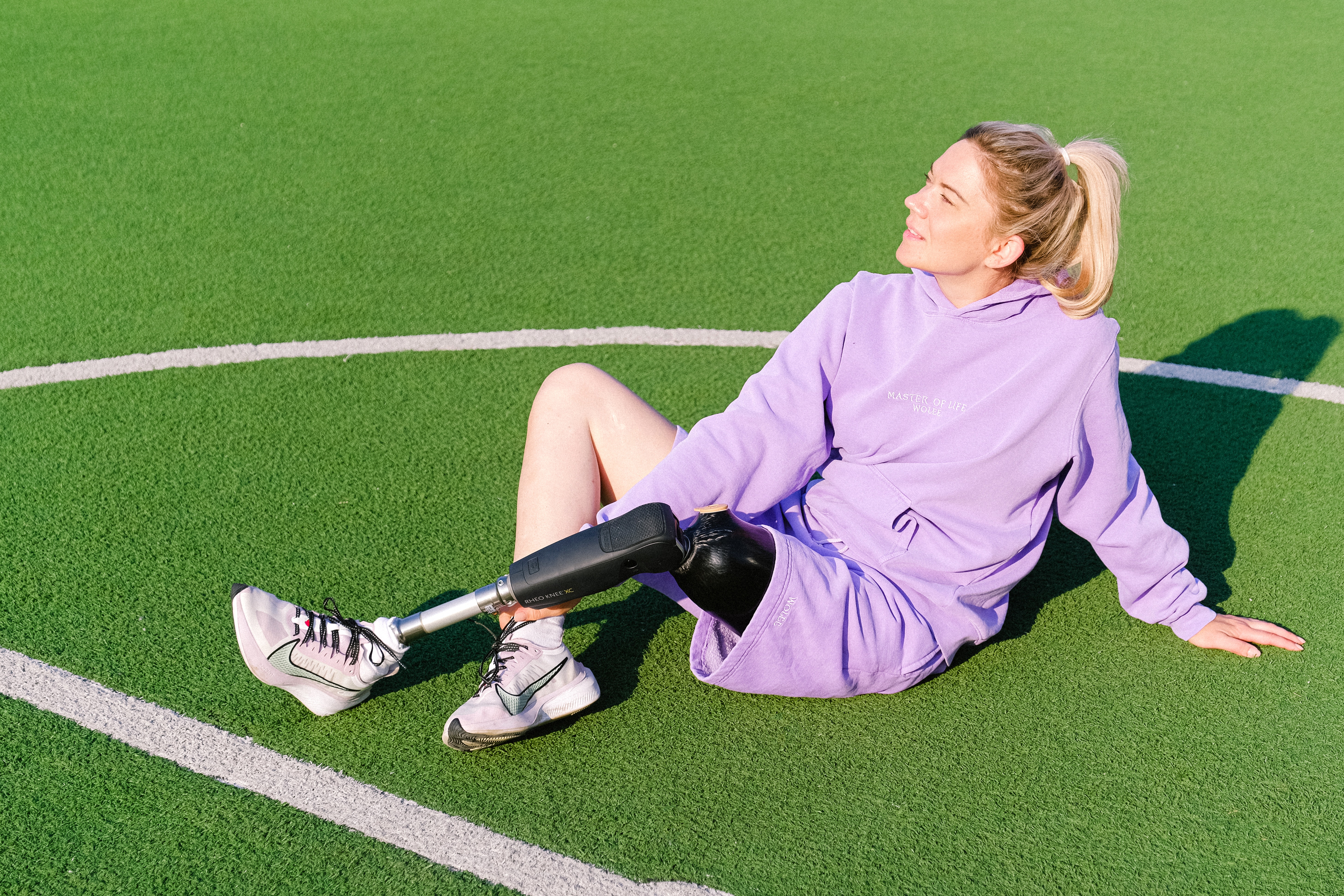 Woman athlete with an artificial left leg sits on a soccer field.